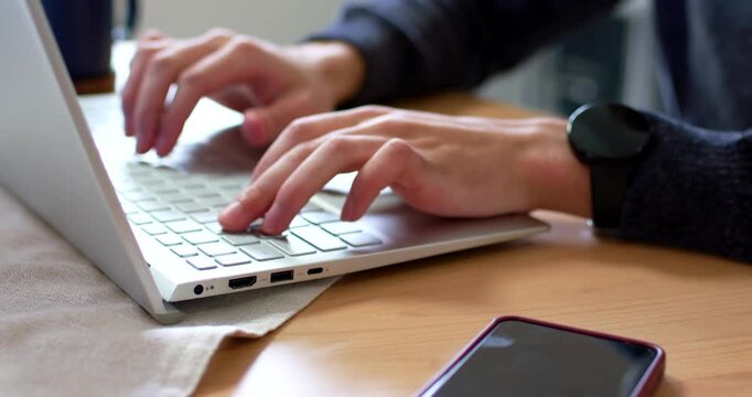 African American man typing with poised hands above keyboard at wooden table, doing work on laptop