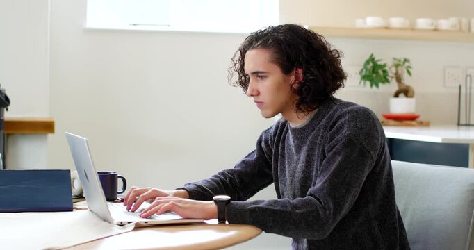 African American man typing on laptop at home tilting screen reaching mug and headphones finishing