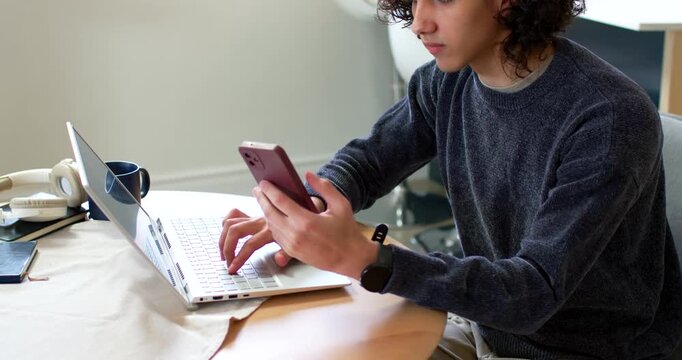 African American man sitting at round table, checking phone, typing on laptop for work, copy space