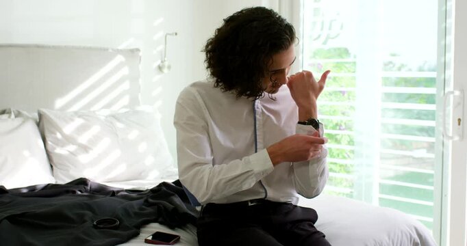After checking watch African American man sitting on bed adjusting strap and shirt cuff before work