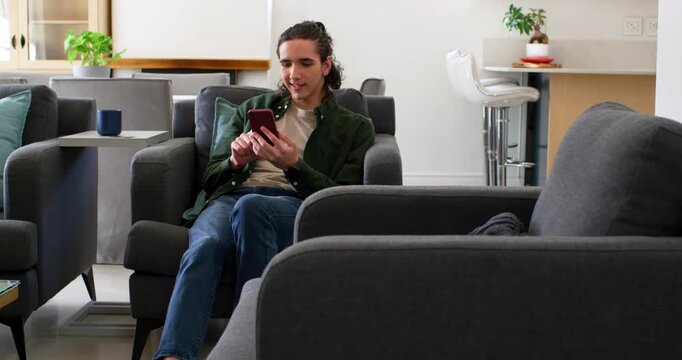 Male in 20s sitting in living-room, tapping red phone, looking left table, reaching card, verifying