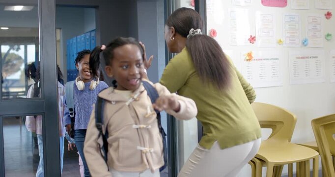 Diverse students entering classroom door, teacher highfiving welcoming girl raising hand, backpacks