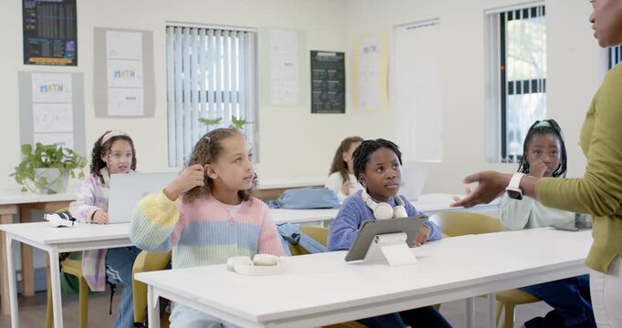 Preteen classmates watching while instructor calling on students, two girls walking with tablet