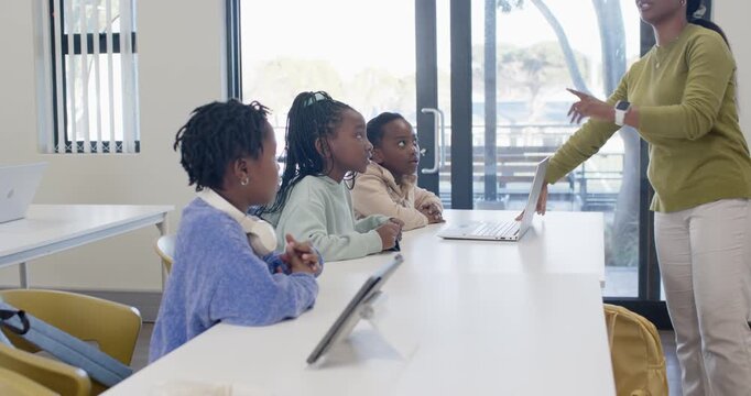 African American teacher with three Youth girls touching laptop, demonstrating at long white table