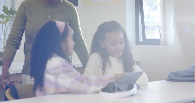 African American teacher guiding two girls in class after tablet taps leaning over pointing to help