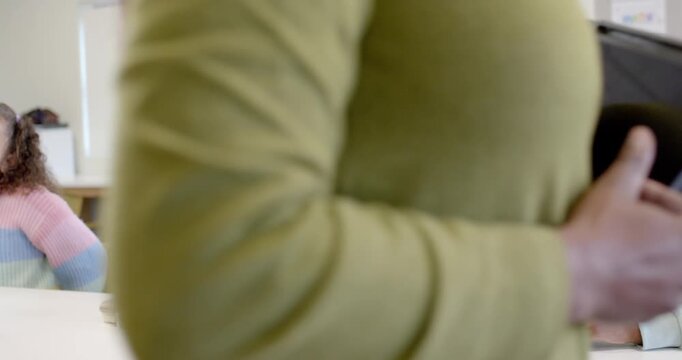 Teacher entering class left with tablet, teaching teen girls; center student mint hoodie listening