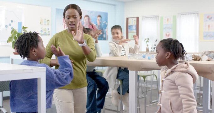 African American teacher raising hand inviting kids to high-five to engage with bottles at school