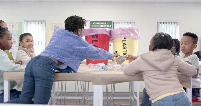 Students at table seeing pile teen in blue sweater leaning sorting bottles into PAPER PLASTIC bins