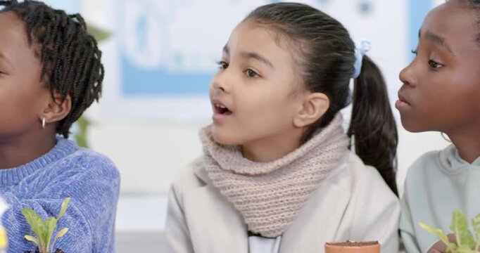 Diverse female teens after chat watching blue teen studying root ball with magnifier at school