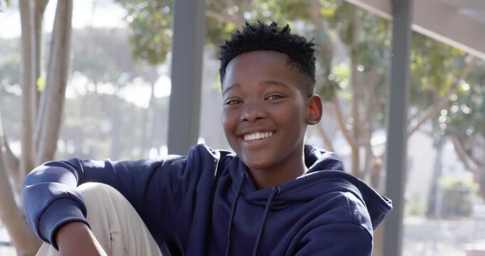 African teen sitting on park bench wearing navy hoodie shifting smiling reacting to off-camera cue