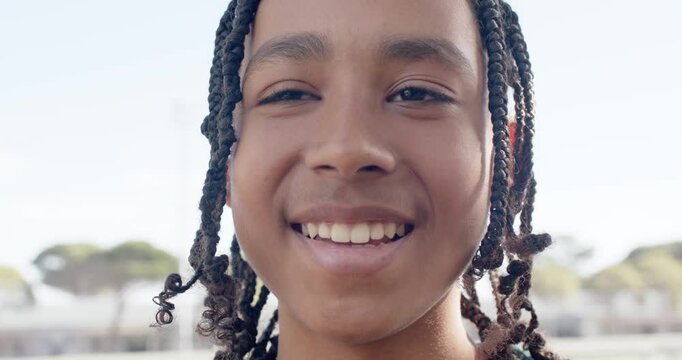 African American teen male responding to unseen cue, smiling and tilting head at park, braided hair