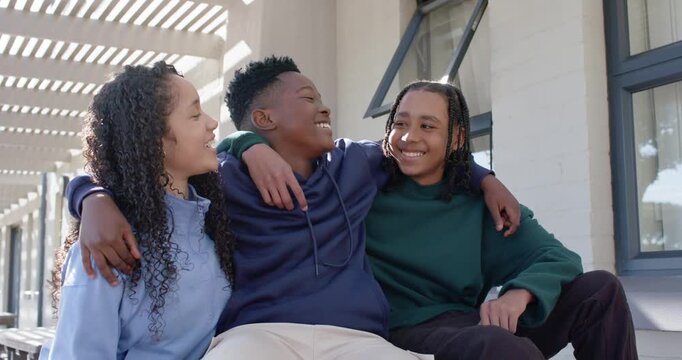 African American teens laughing, leaning on bench in hoodies under pergola, answering friend call