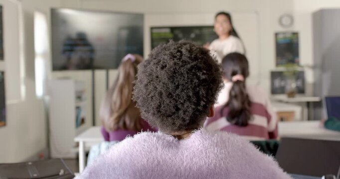 African American teen student watching teacher gesturing at board, monitor in class to learn