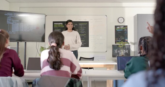 Indian woman instructor gesturing, responding to raised hand in class with code screen and laptops