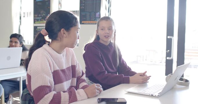Diverse teenagers turning toward peer, collaborating on project in class using laptop smartphone