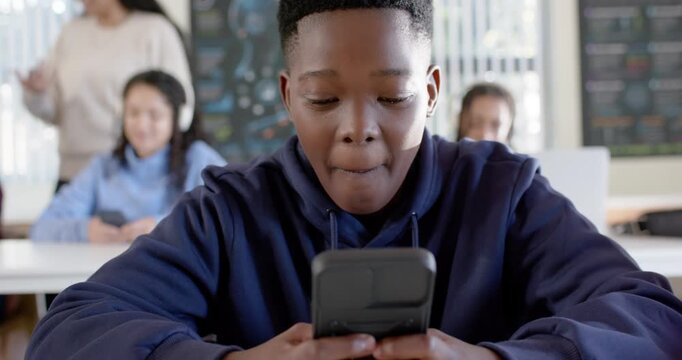 Teenage male student at classroom desk phone buzzing, tapping phone, smiling while teacher speaking