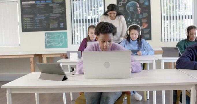 African American youth in lab reaching tablet raising hand seeking help on laptop teacher gesturing