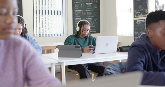 Diverse teens, male teen in green shirt scrolling smartphone, glancing at laptop for class at desks