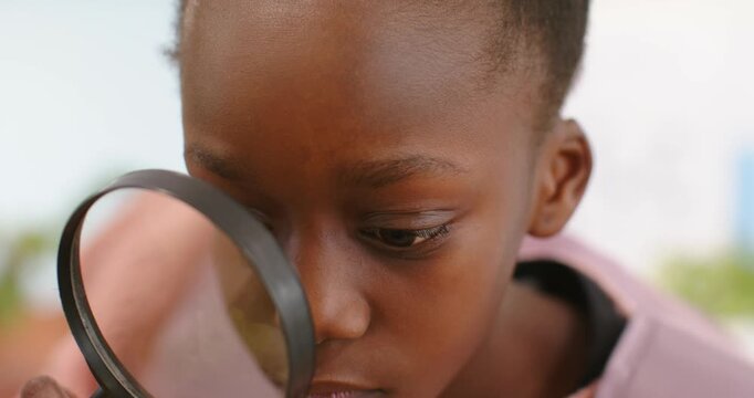African female child bringing black-rim magnifying glass toward nose, inspecting in soft interior