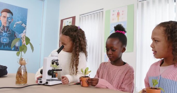 Three African-American girls operating microscope holding pot during science class examining roots