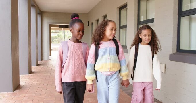 African American schoolgirls walking toward doorway on school corridor, with backpacks, chatting