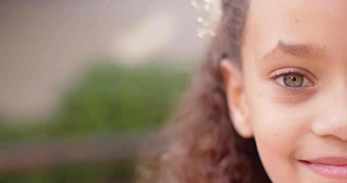 Female child curly hair blinking and smiling while camera pulling back by garden fence, copy space