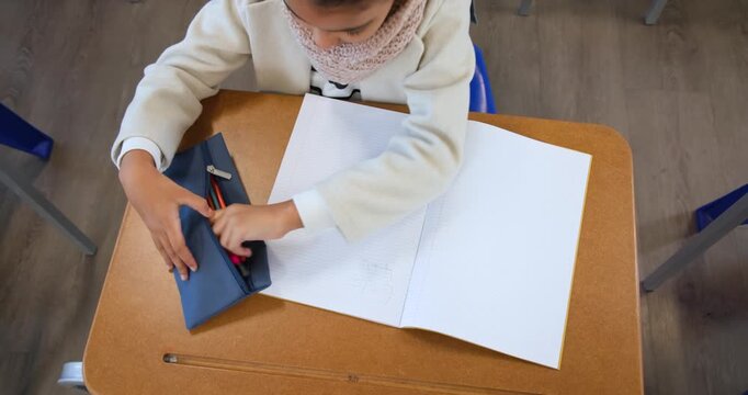 African teenage girl unzipping case, selecting pink pencil, tracing hand, making art at school desk