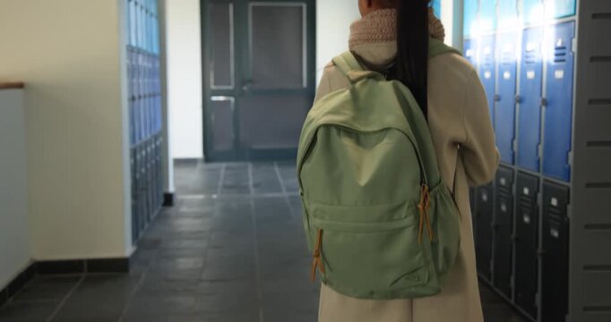 African American teen student walking corridor toward door with green backpack, pausing, listening
