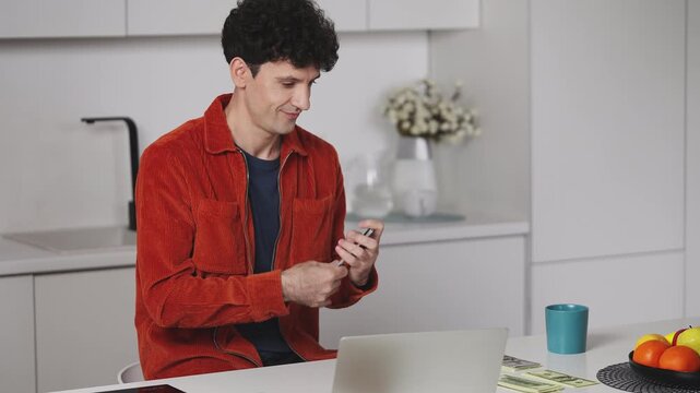 Smiling male IT developer counting cash in front of laptop, pleased with income