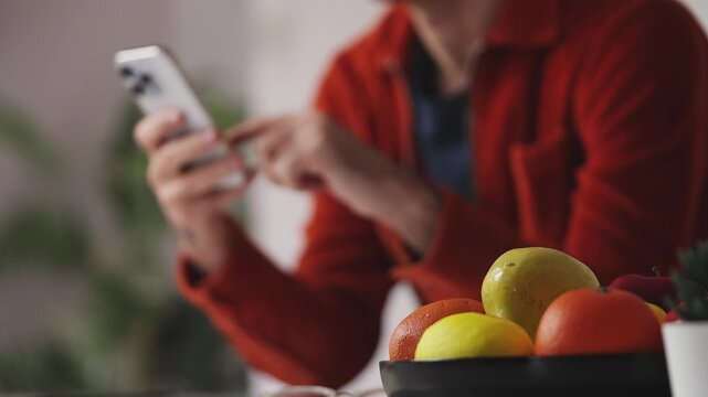 Young male scrolling photos in social network app on cellphone in kitchen, rest
