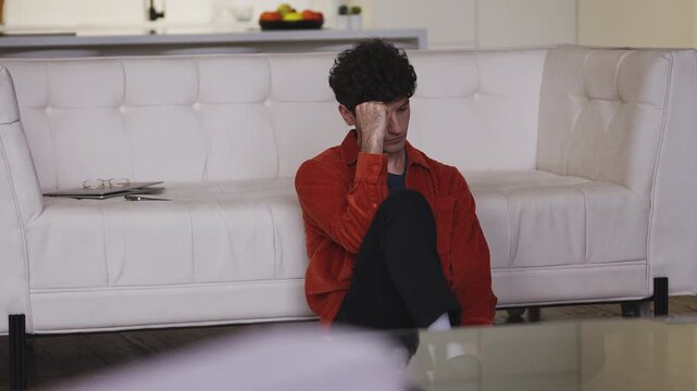 Desperate young man thinking about family problems while sitting on the floor