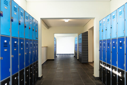 Locker corridor featuring blue upper, dark lower lockers, locks, vents, tiled hall leading to door