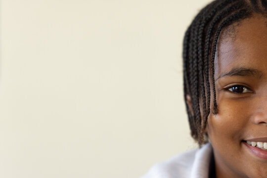 African adolescent male smiling and posing on right side against beige wall with braids, copy space