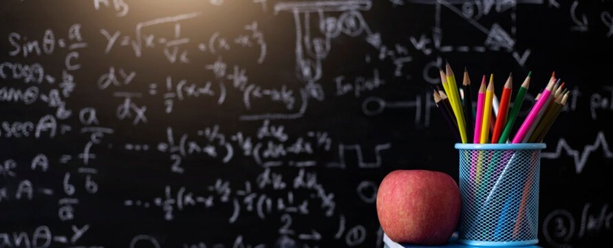 Blackboard filled with complex math equations. Colorful pencils rest in a mesh holder. Red apple sits beside the pencil holder. Scene suggests student or teacher preparation