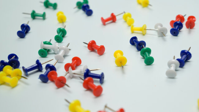 multicolored push pins arranged on white background top down view