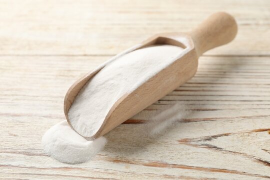 Baking soda in scoop on color wooden table, closeup