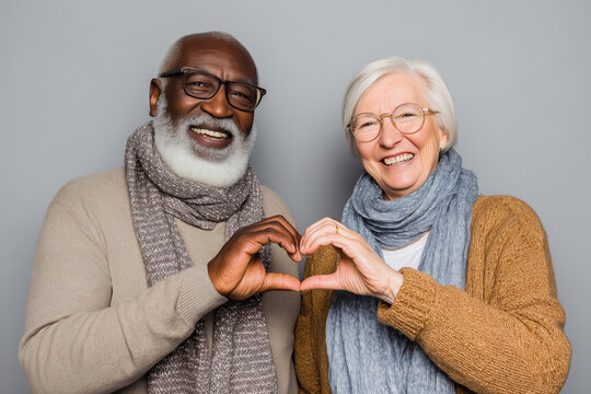 Happy diverse elderly couple smiling and making a heart shape with their hands.