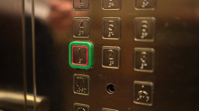 Close-up of female hand with French manicure pressing illuminated green first floor button on modern steel elevator control panel with braille for visually impaired people. Shooting in slow motion.
