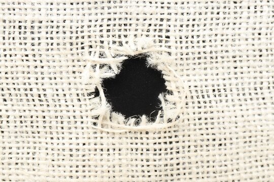 Burlap fabric with torn hole on black background, top view
