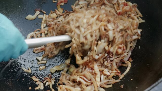 Overhead view shows sliced onions tossed in dark wok, with caramelized strands, glossy oil and rising wok