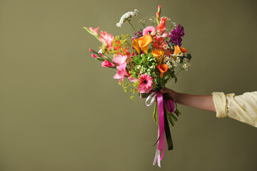 Obraz premium Woman with bouquet of beautiful vibrant flowers on olive background, closeup. Space for text