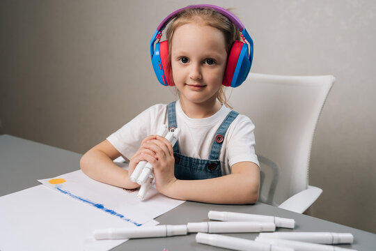 Portrait of focused child in headphones creating art with markers. Calm, creative kid learning at home. Neutral background with copy space. Concept for education, hobby, development..