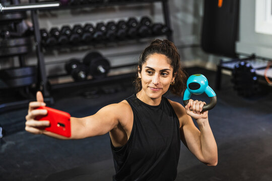 Woman exercising with kettlebell and recording video in gym