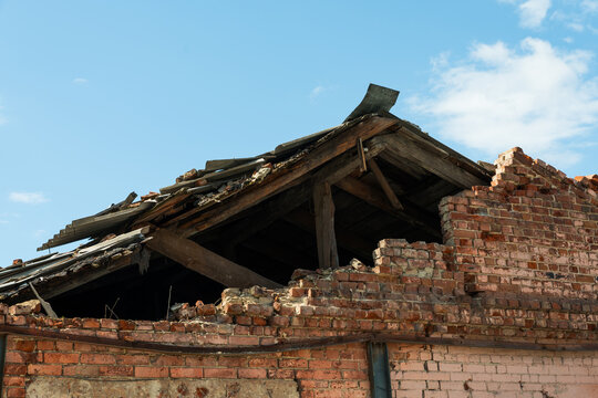 Destroyed roof and collapsed brick wall of an old abandoned building against a blue sky with clouds