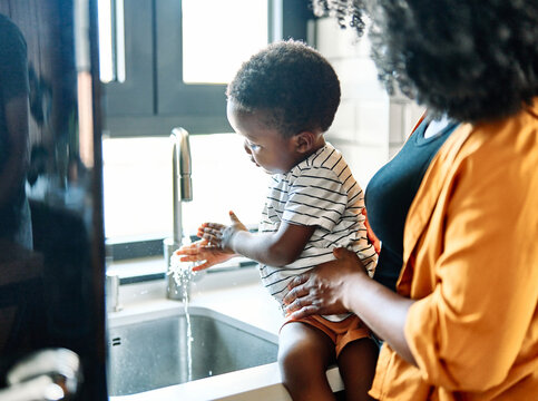 Portrait of a little black boy and his mother washing hands, mother helping and teaching her son hygiene and good habits and routines, at home