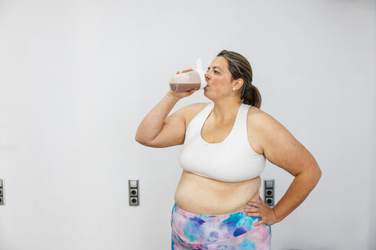 Curvy woman drinking protein shake after workout session