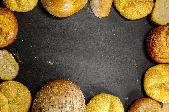 An assortment of bread rolls frames a dark background, leaving empty space in the center for text, ideal for bakery promotional designs