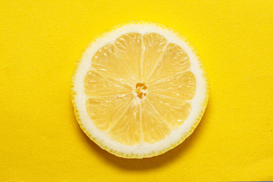 A single lemon slice rests on a bright yellow background, its detailed segments and texture creating a vivid monochromatic composition