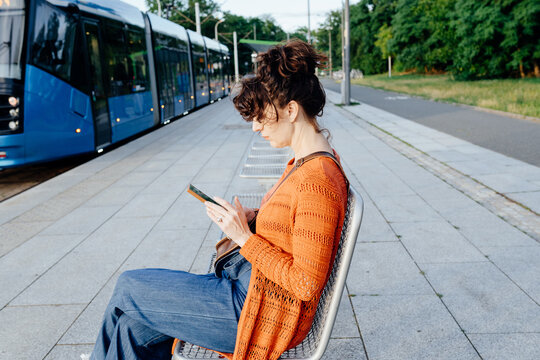Focused female commuter using smartphone while seated beside Focused female commuter using smartphone while seated beside modern city tram