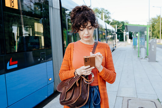 Focused young woman checking mobile travel information beside city tram